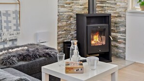 Ein modernes Wohnzimmer mit Steinwand, einem schwarzen Kaminofen, einer Couch und einem Couchtisch mit Buch und Gläsern.