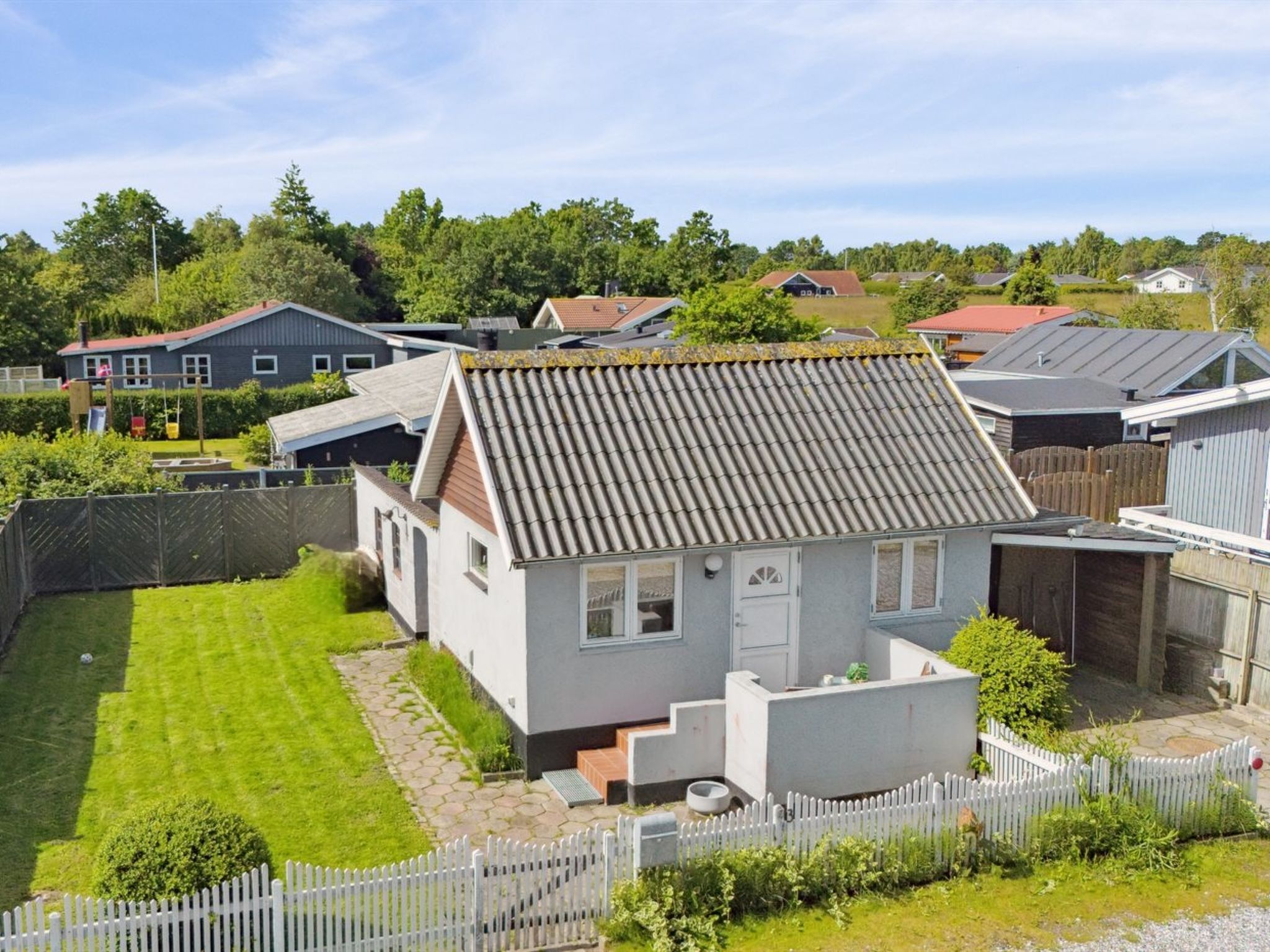 Een woonwijk met een huis, voorzien van een pannendak, een kleine voortuin en een witte picket fence.
