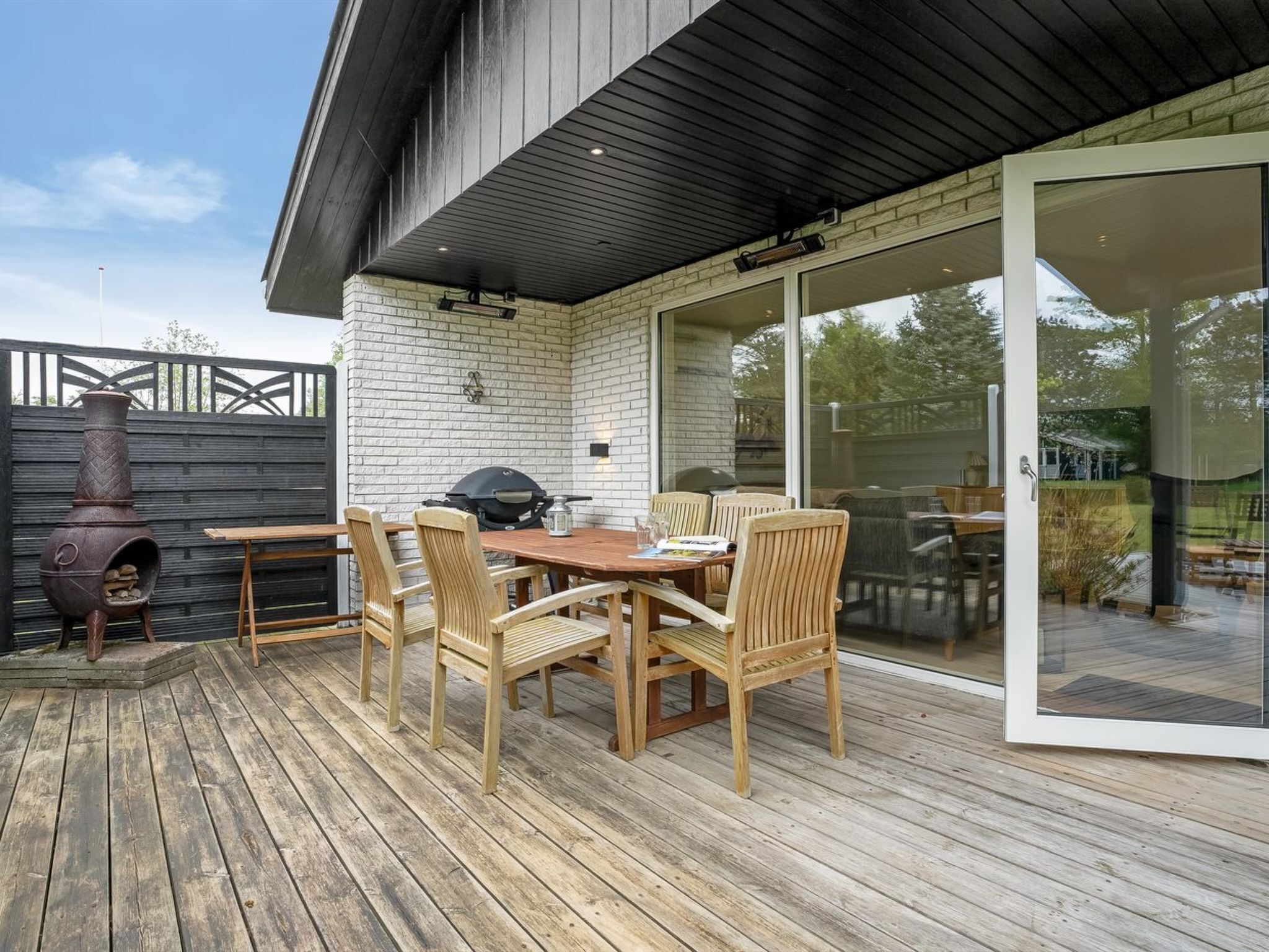 An outdoor patio with a wooden deck, a brick wall, and a glass door leading to a garden.
