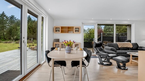 A modern living room with a dining area, large windows, and a view of the outdoors.