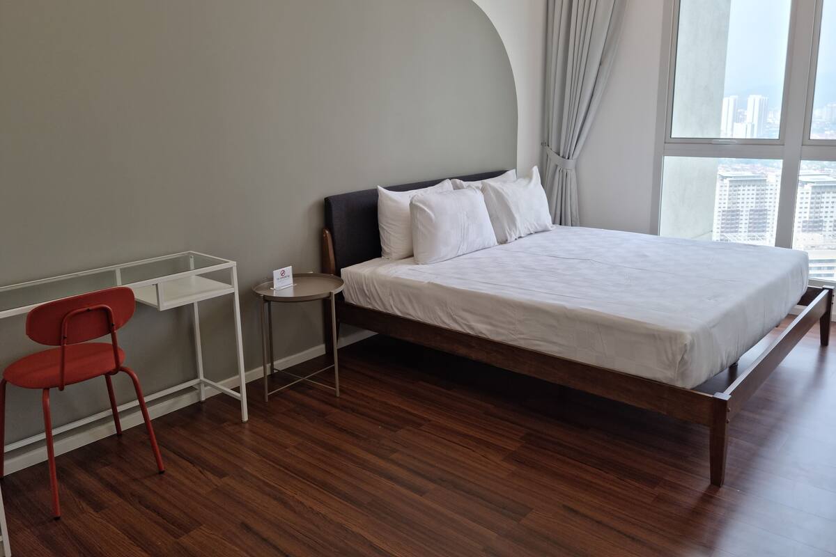 A modern hotel room with a wooden floor, a single bed with white bedding, a red chair, and a small side table.