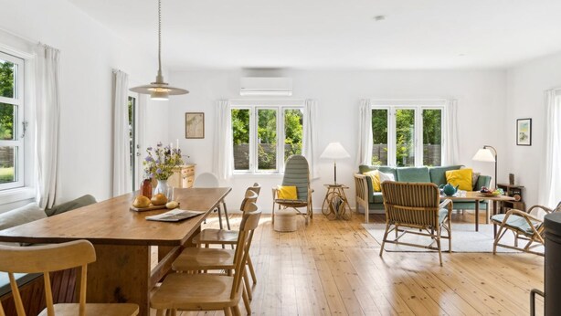 A spacious living area with a wooden dining table, chairs, a sofa, and a coffee table. There are windows providing natural light and views of greenery outside. - "Heidl" - 1.3km to the fjord by Interhome (Rørvig)