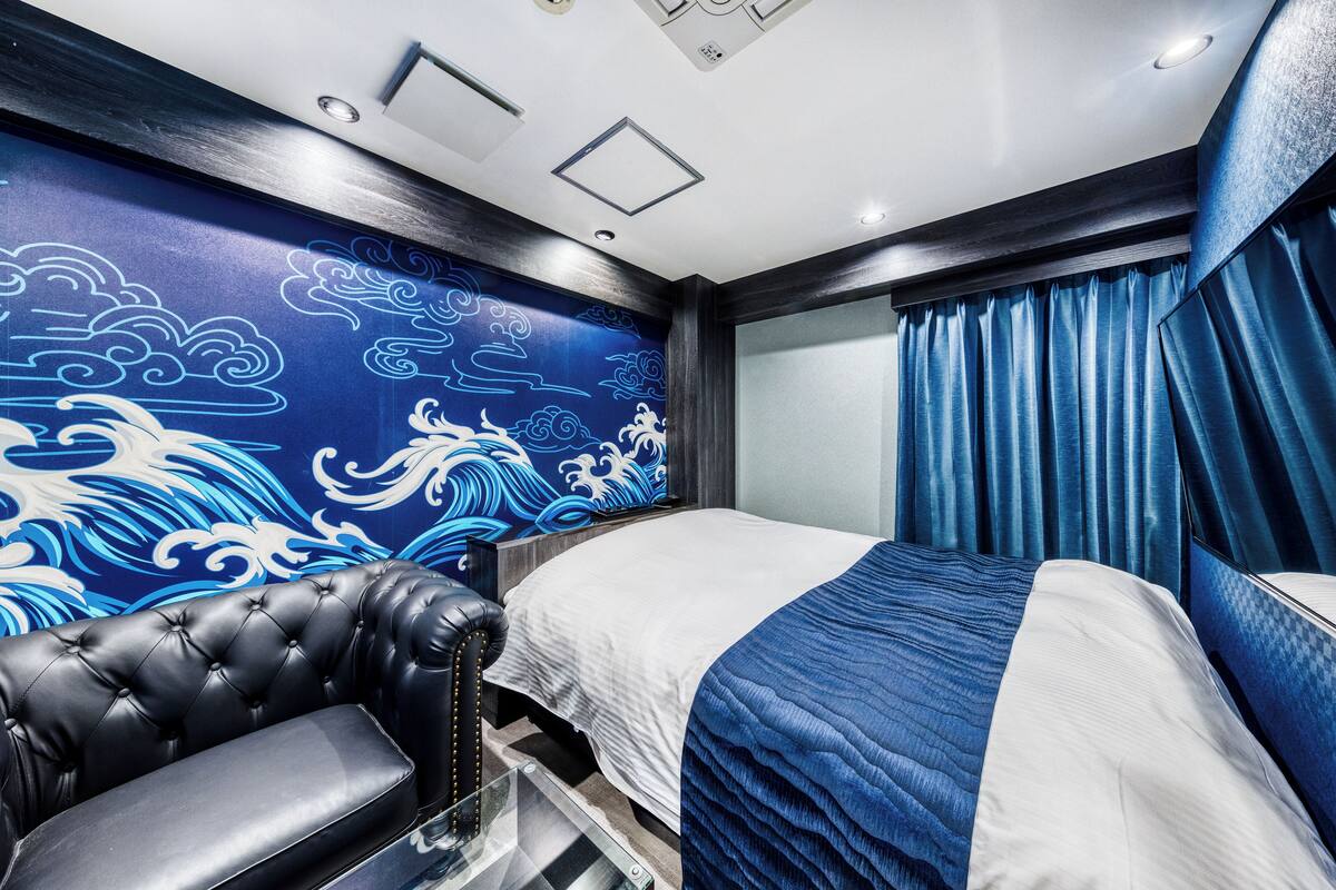 Una habitación de hotel con una cama, un sillón de cuero y una pared con un diseño de olas azules y blancas.