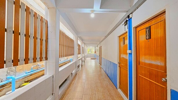 Un long couloir, avec des portes en bois sur le côté droit, chacune portant un numéro.