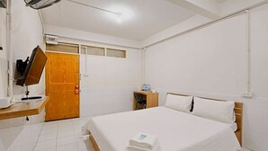 Une chambre d’hôtel avec un lit, une porte en bois, un bureau avec une chaise, une télévision et une petite table avec une lampe.