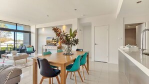 Un comedor moderno con una mesa de madera y sillas color turquesa, un florero con plantas y vistas al exterior a través de ventanas amplias.
