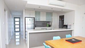 Una cocina moderna con armarios blancos, una isla central y un comedor con mesa de madera y sillas azules.