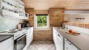 Une cuisine compacte avec des meubles blancs, une cuisinière, un four à micro-ondes et une fenêtre donnant sur un espace verdoyant.