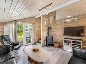 En moderne stue med en stenvægspejs, et fladskærms-tv, lædersofaer og en glasdør, der fører ud til en terrasse.