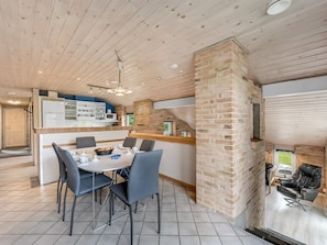 A modern kitchen with a central island, a dining area with a round table and chairs, and a brick fireplace.