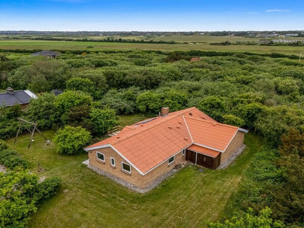 A house with a red roof, surrounded by lush greenery and a clear sky.