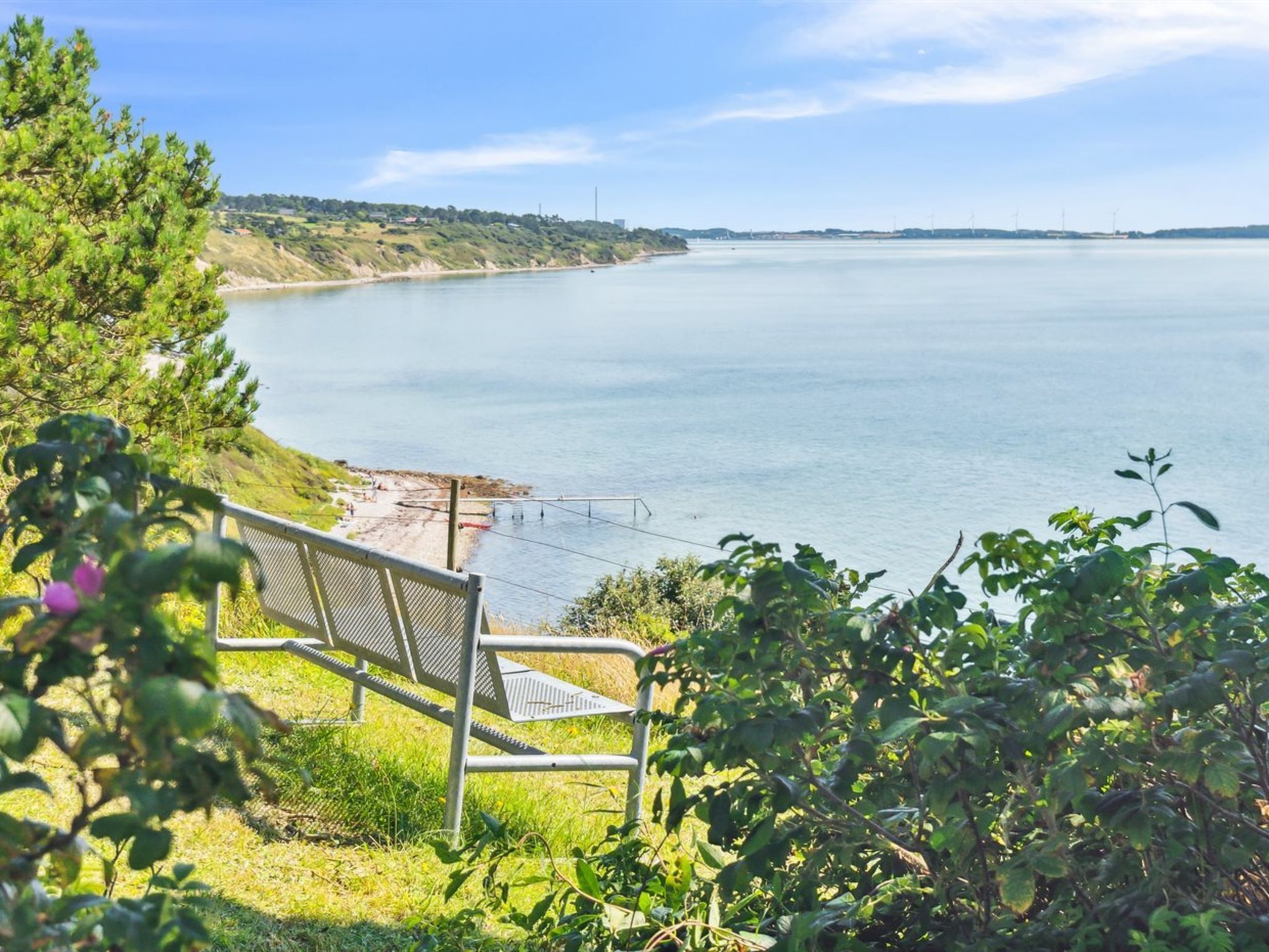 A bench overlooking a calm body of water with a distant shoreline and greenery.