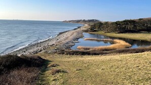 A coastal landscape with a pebbly beach, a calm water body, and a grassy area with trees. - "Uschi" - 86m from the sea by Interhome (Kalundborg)