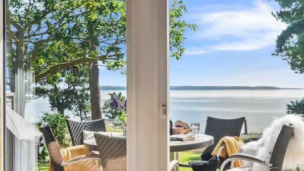 A patio with wicker chairs and a table, overlooking a lake with a clear view of the water and distant land. - "Uschi" - 86m from the sea by Interhome (Kalundborg)