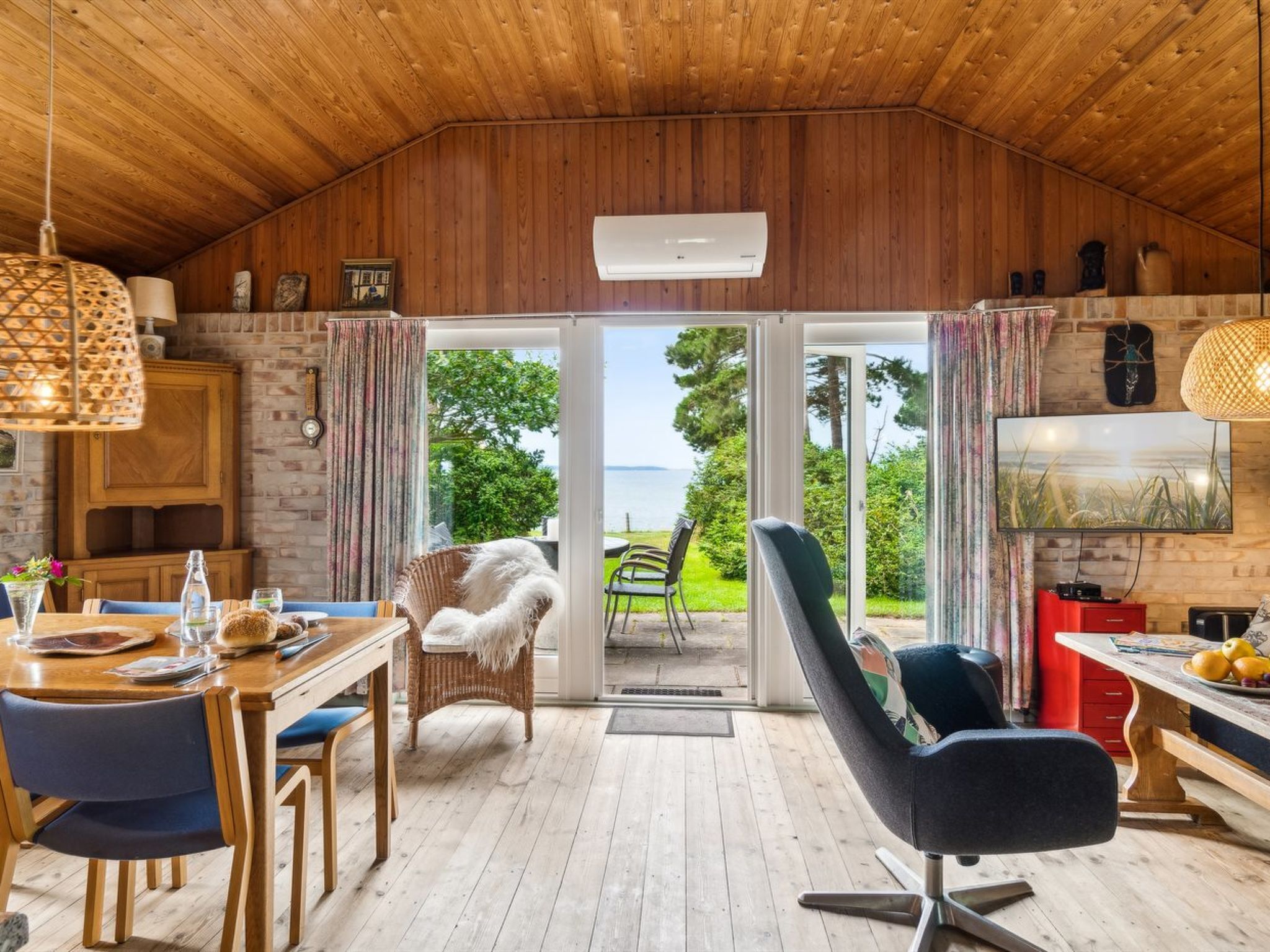 Ein gemütliches Blockhaus-Interieur mit Holzbalkendecke, Essbereich, bequemer Sitzgelegenheit, Fernseher und Blick ins Freie.