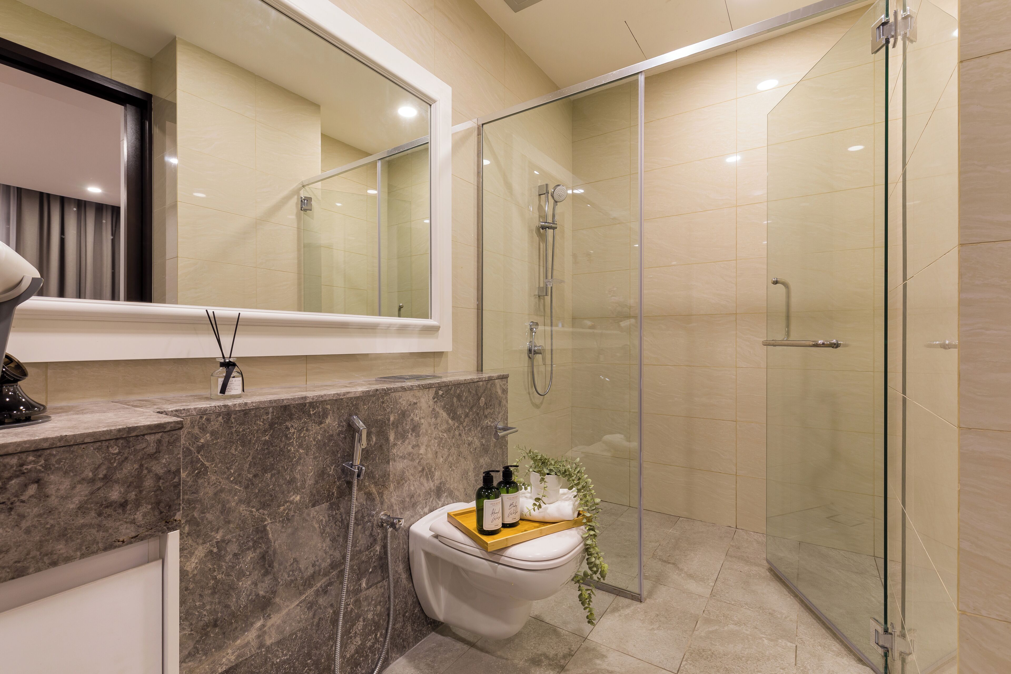 A modern bathroom with a glass-enclosed shower, a marble vanity, and a toilet with a tray of toiletries.