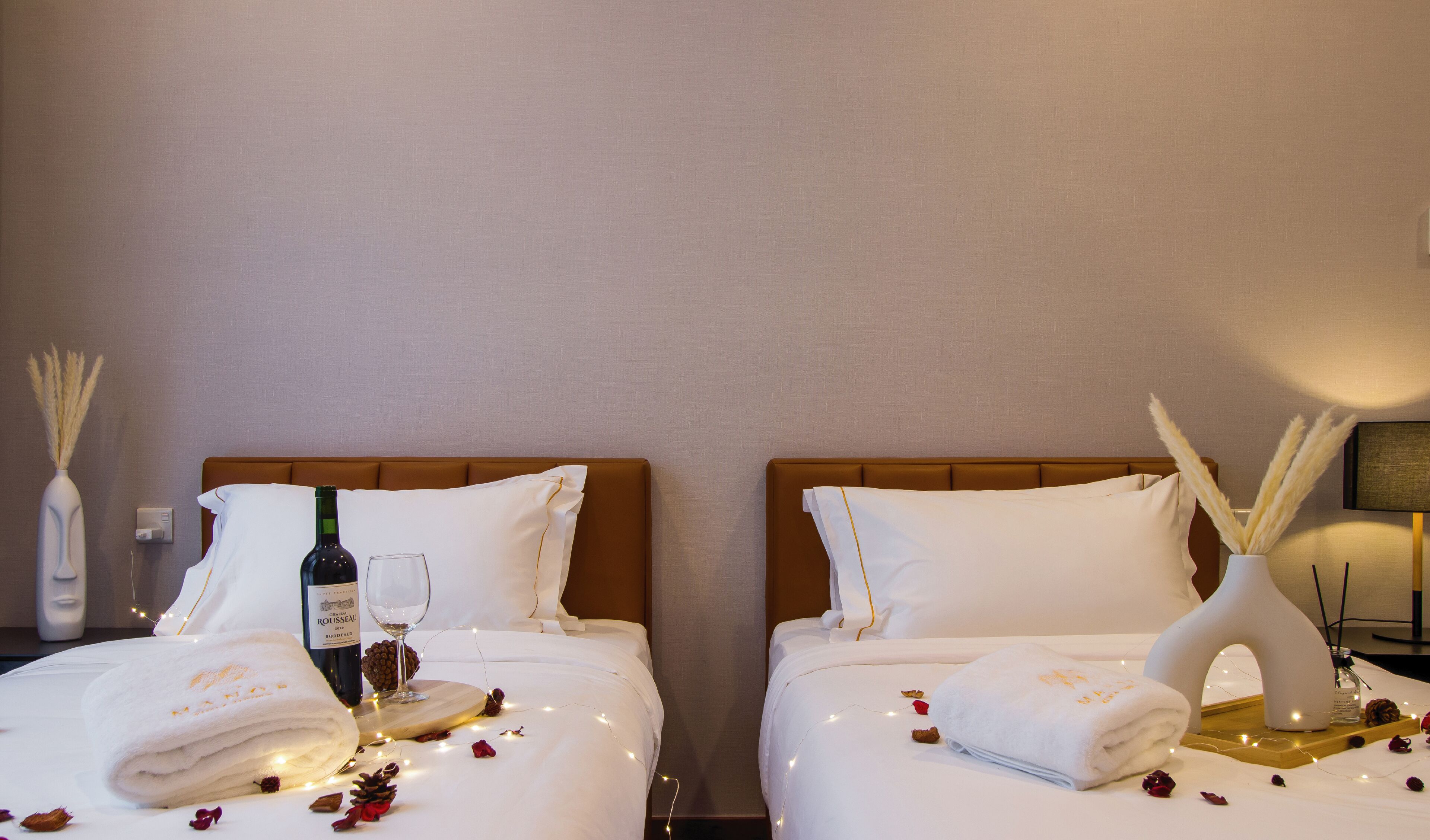 Ein Hotelzimmer mit zwei Betten, jeweils mit weißen Bettwäsche, einer Weinflasche und einem Glas auf einem Holztablett.
