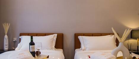 Ein Hotelzimmer mit zwei Betten, jeweils mit weißen Bettwäsche, einer Weinflasche und einem Glas auf einem Holztablett.