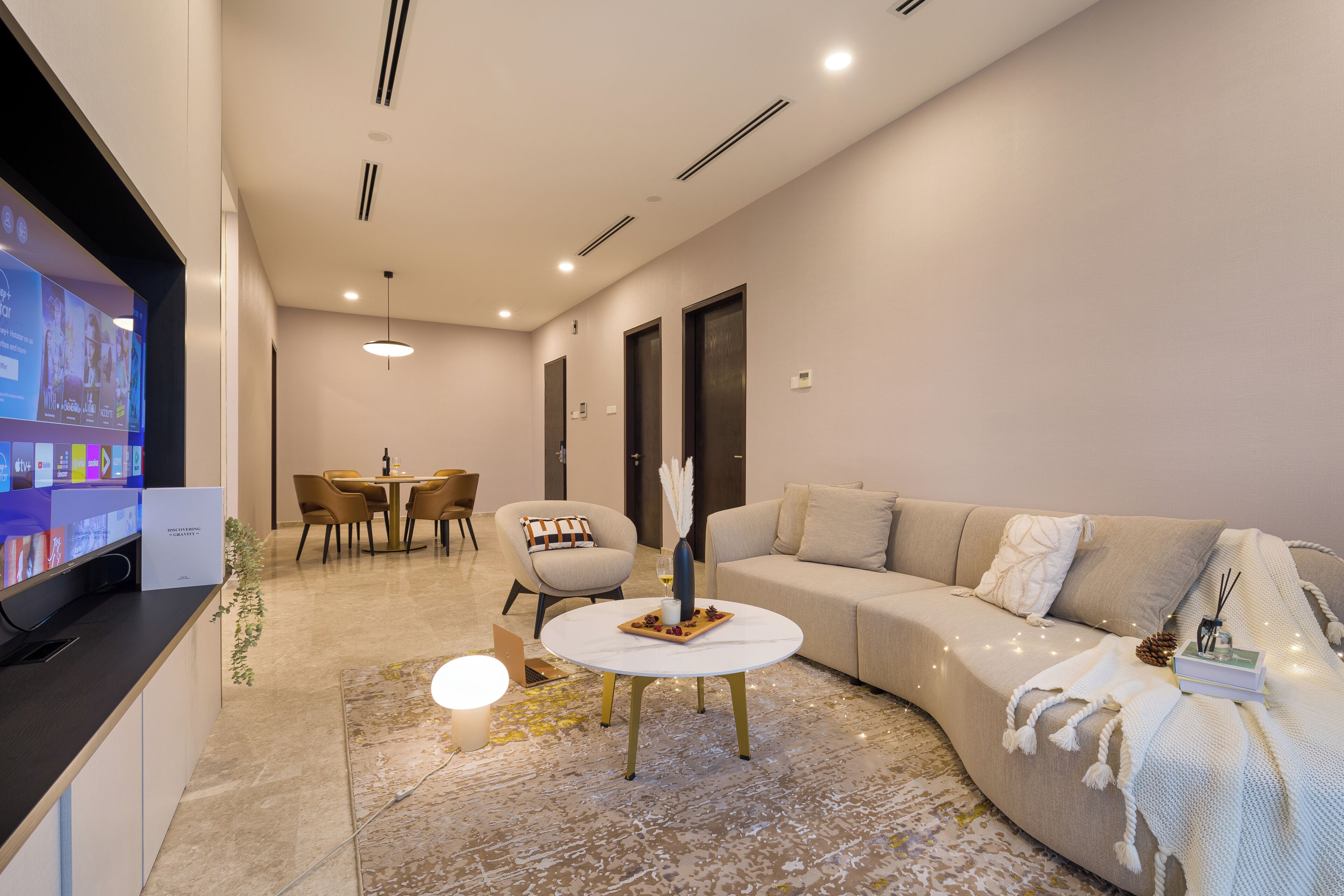 A modern living room with a sofa, a coffee table, a TV, and a dining area with chairs and a table.
