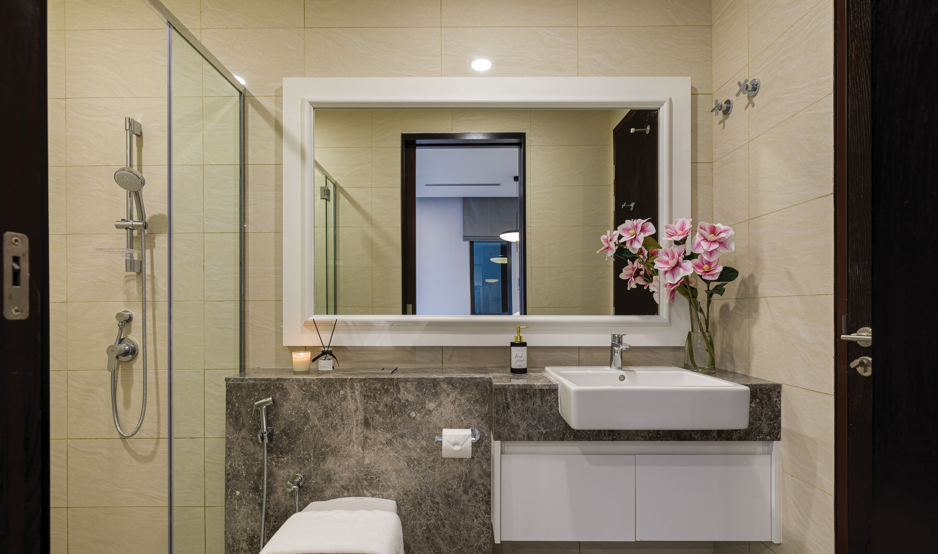A modern bathroom with a glass-enclosed shower, a white toilet, a sink with a marble countertop, and a mirror above the sink.
