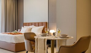 A hotel room with a bed, a dining table with chairs, and a bedside table with a lamp.