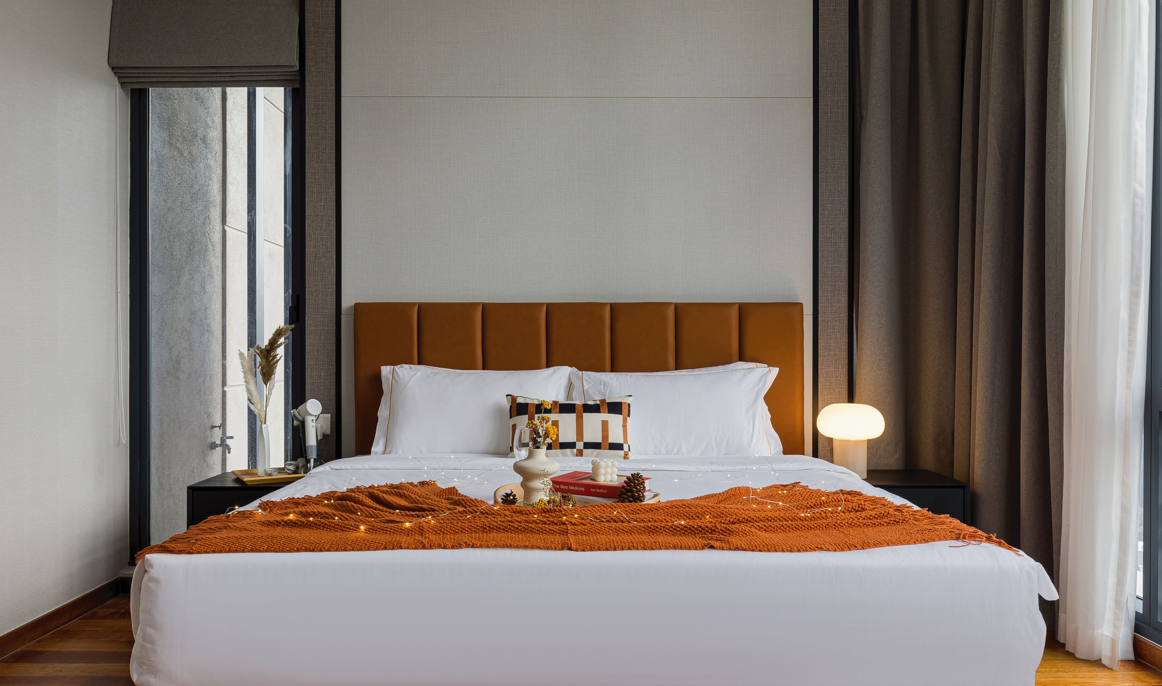 Een keurig opgemaakt bed met een witte dekbedovertrek, een bruin hoofdbord en een sierkussen.