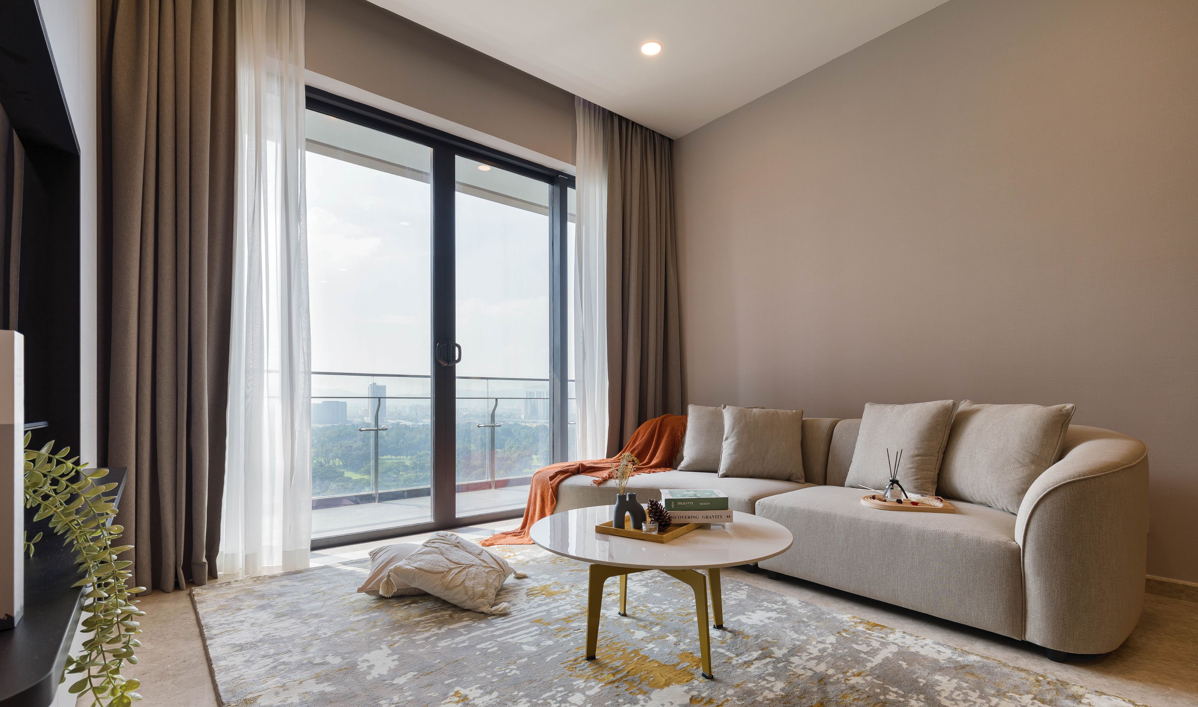 A modern living room with a sofa, a coffee table, and a view of the city through large windows.