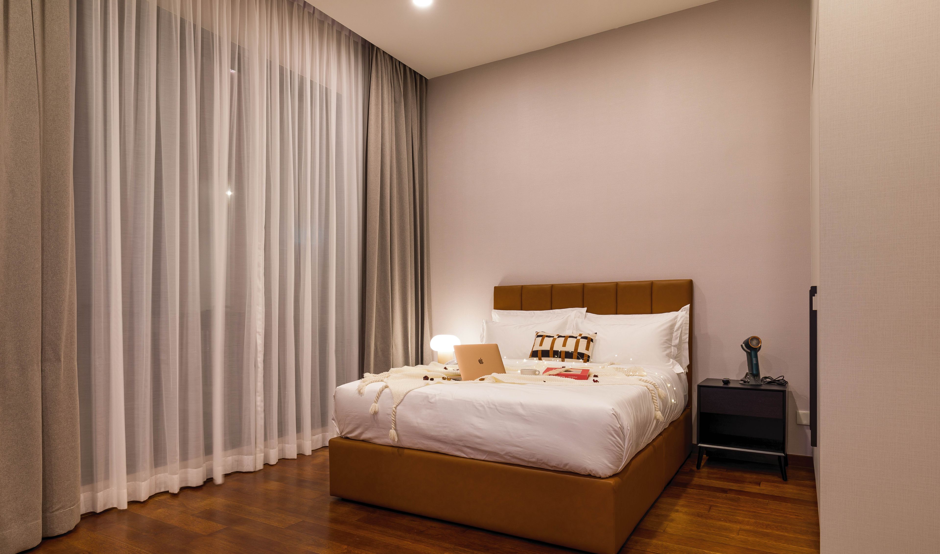 A neatly made bed with a laptop, pillows, and a bedside table with a lamp.