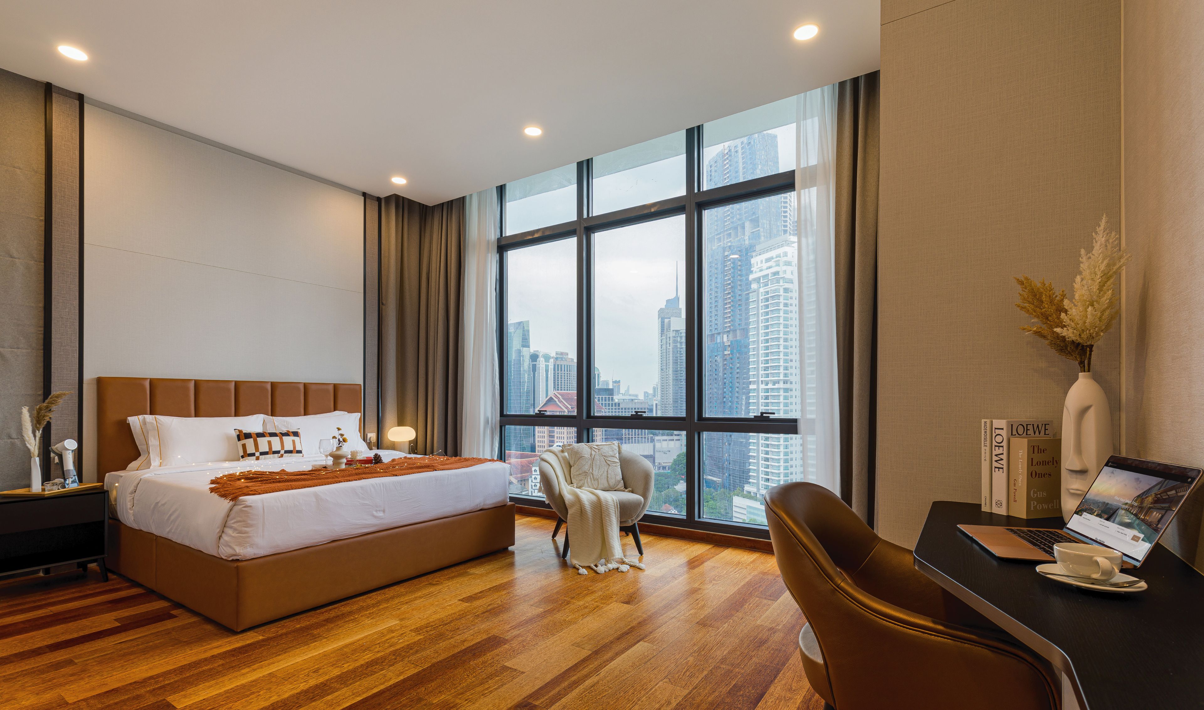 Une chambre d’hôtel moderne dotée d’un grand lit, d’un bureau avec un ordinateur portable et offrant une vue sur la ville grâce à de grandes fenêtres.