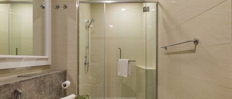 A modern bathroom with a glass-enclosed shower, a toilet with a towel and a plant beside it, and a mirror above the sink.