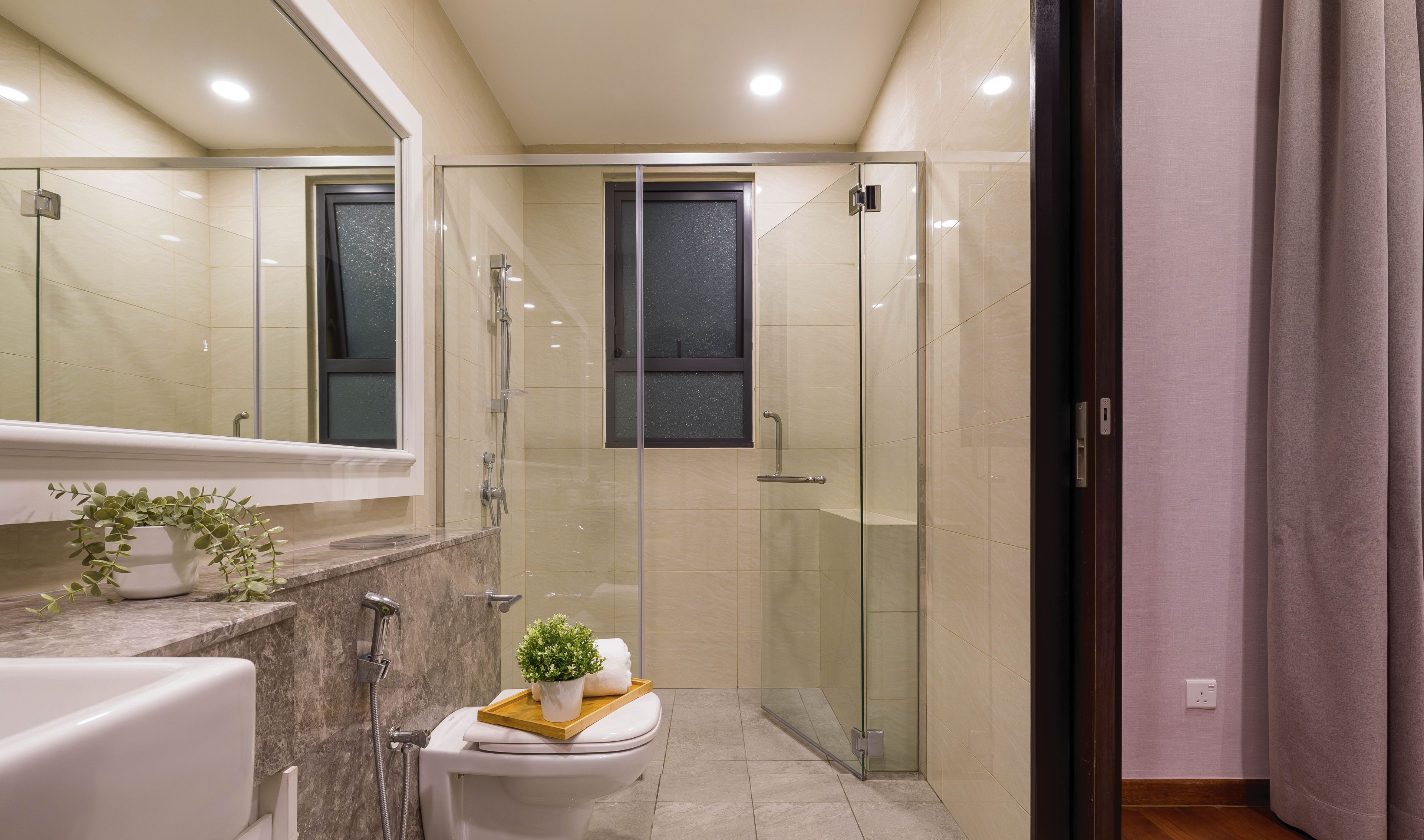 A modern bathroom with a glass-enclosed shower, a toilet with a small plant on the lid, and a bathtub.