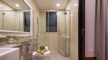 A modern bathroom with a glass-enclosed shower, a toilet with a small plant on the lid, and a bathtub.