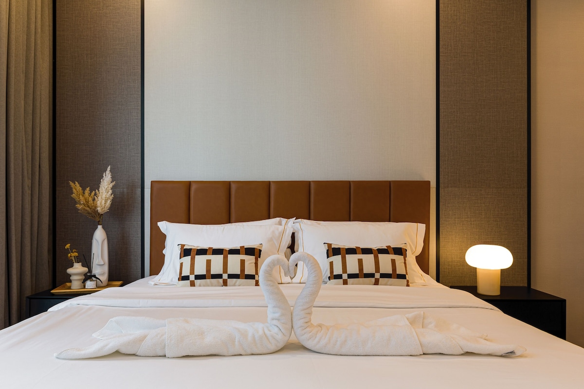 A hotel room with a neatly made bed, a bedside lamp, and a decorative vase with dried flowers.