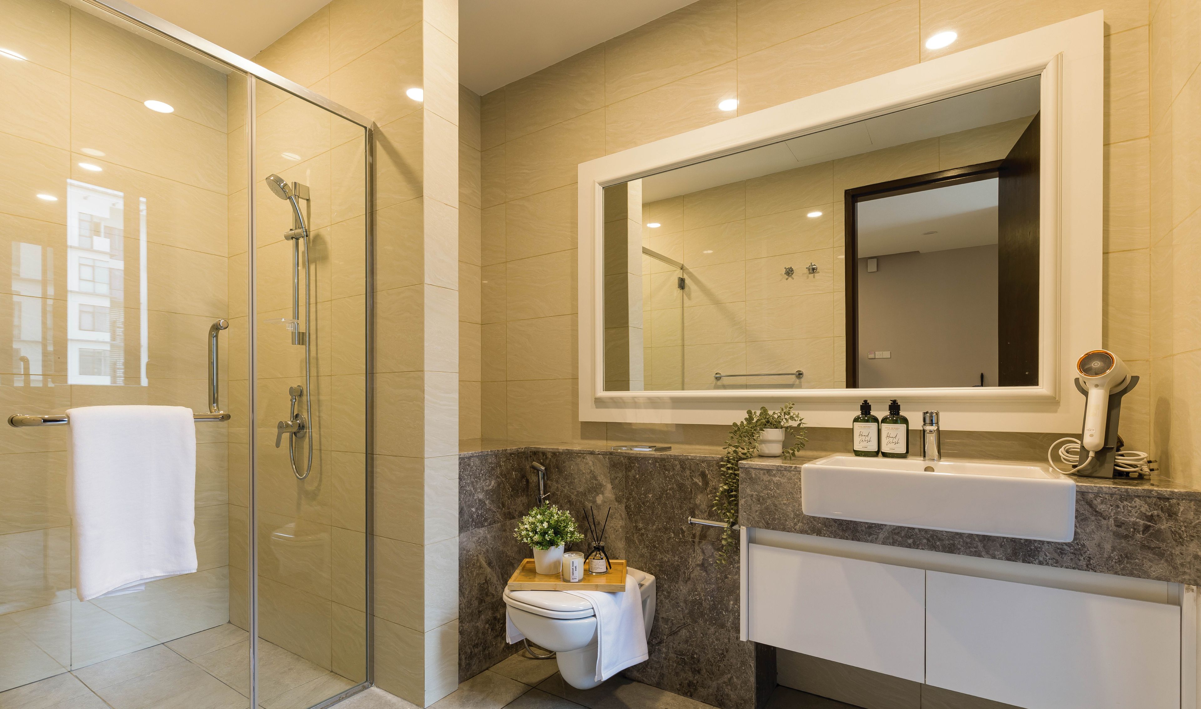 Une salle de bain moderne dotée d’une douche à parois de verre, d’un grand miroir et d’un meuble-lavabo avec un évier et un plan de travail.