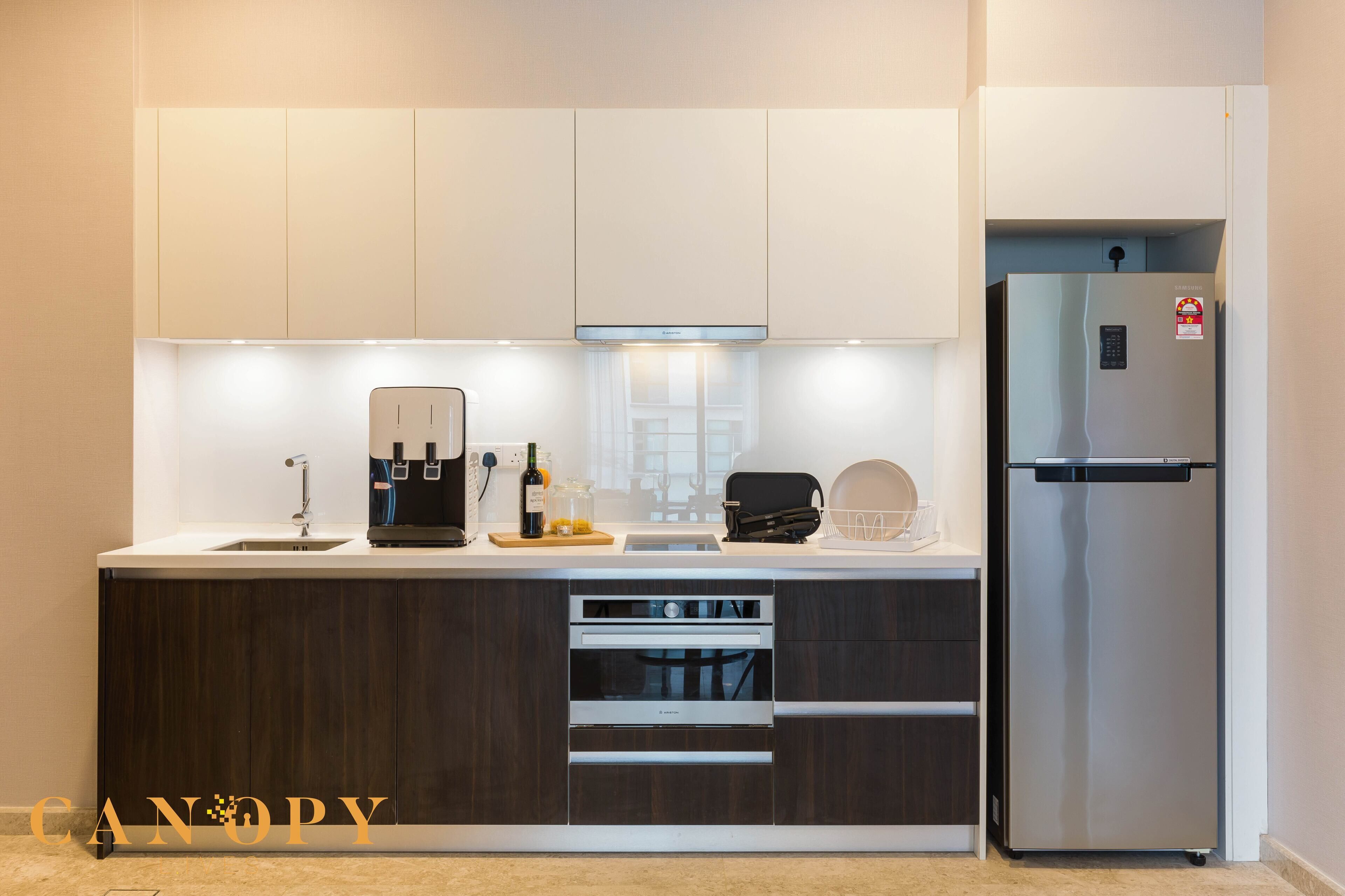 A modern kitchen with a built-in oven, a stainless steel refrigerator, and a countertop with a coffee maker and a wine bottle.