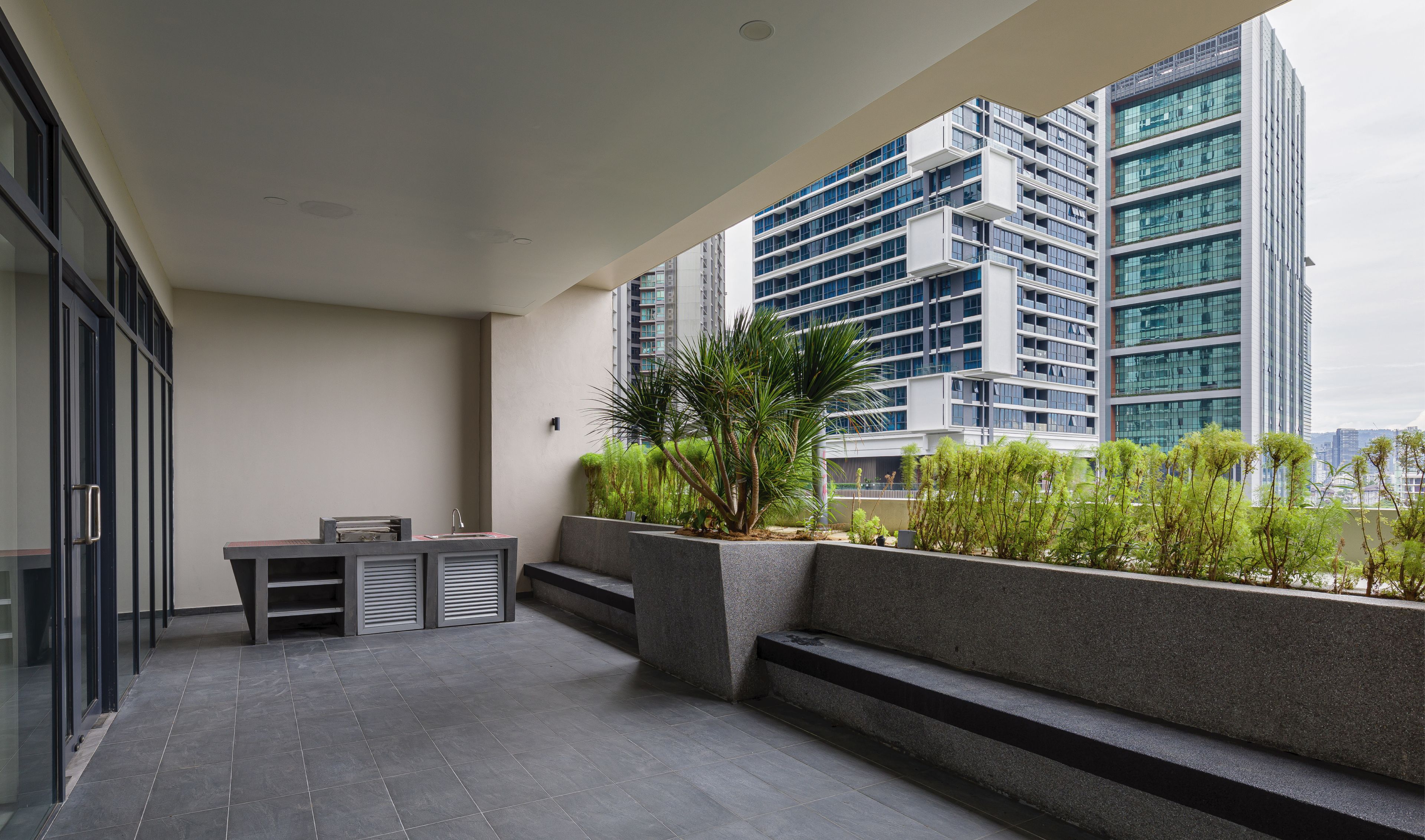 A modern outdoor area with a seating arrangement, a planter with greenery, and a view of high-rise buildings.