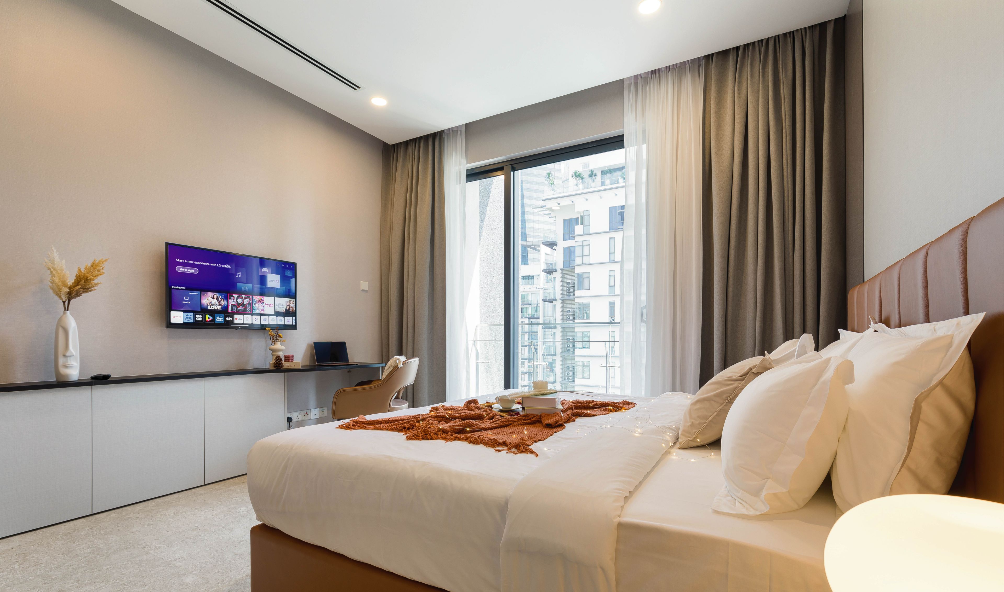 Et moderne hotelværelse med en stor seng, et fladskærms-tv på væggen, et skrivebord med stol, samt udsigt over byen fra vinduet.