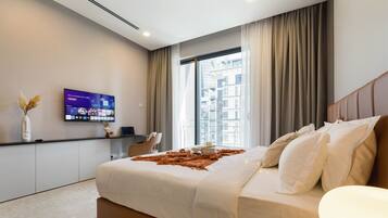 Et moderne hotelværelse med en stor seng, et fladskærms-tv på væggen, et skrivebord med stol, samt udsigt over byen fra vinduet.