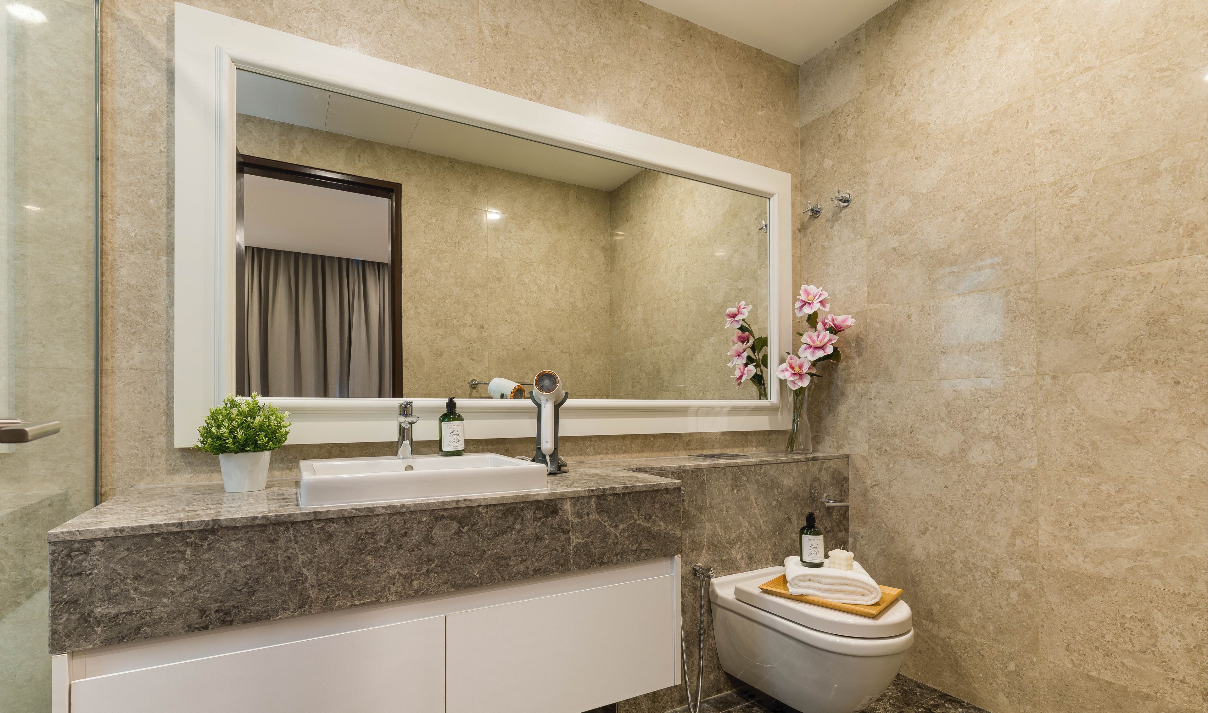 Un baño moderno con lavamanos de mármol, un espejo grande y un inodoro.
