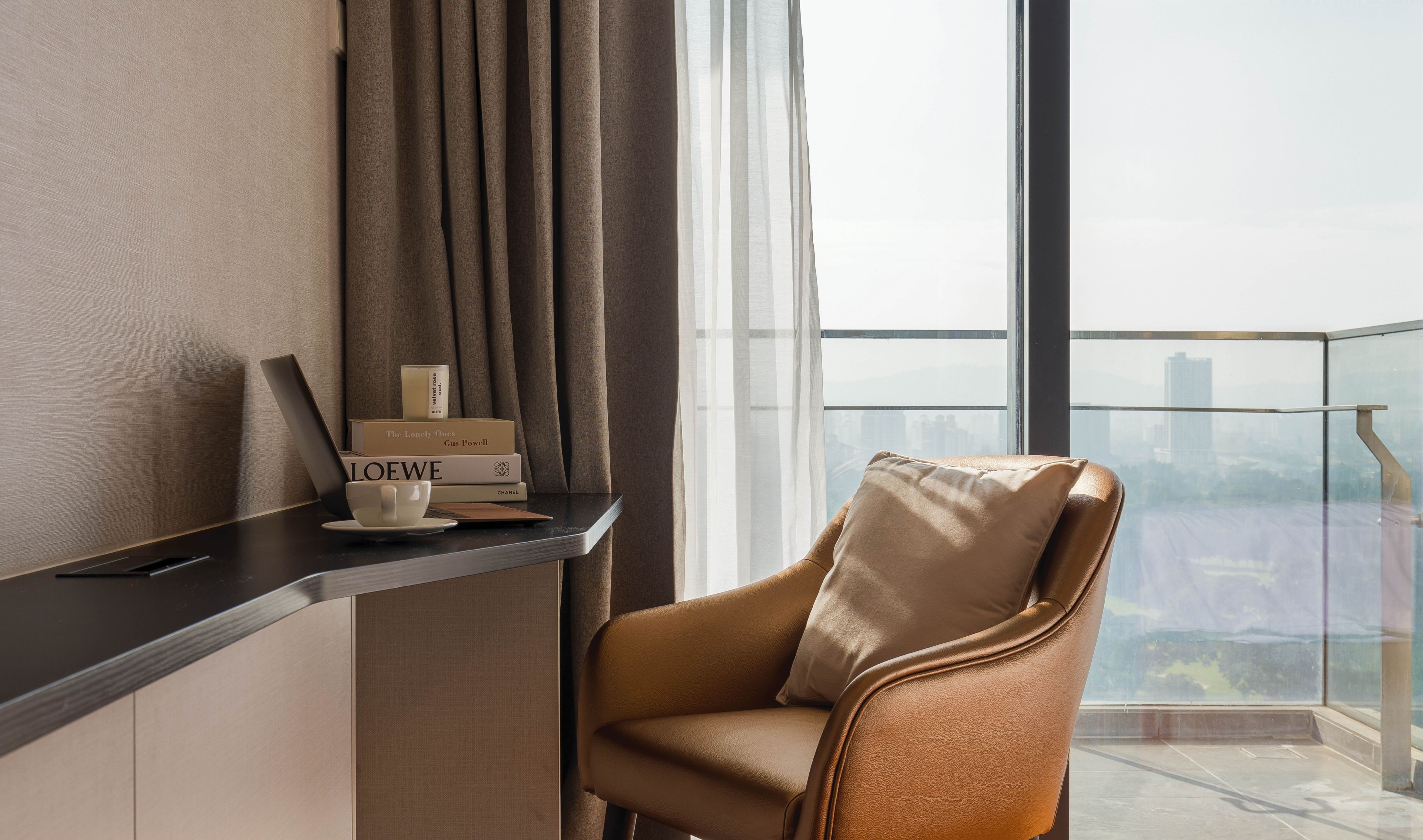 Ein modernes Zimmer mit Ledersessel, Schreibtisch mit Laptop und Blick auf eine Stadtlandschaft durch große Fenster.