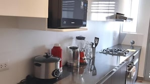 A modern kitchen with a stainless steel countertop, a microwave, a stove, a blender, and a kettle. - Departamento con Vista al Mar (Lima)
