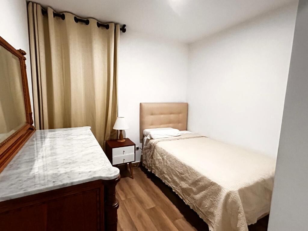 Un dormitorio pequeño y ordenado con una cama individual, una mesita de noche, un espejo y un aparador de madera.