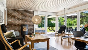 A modern living room with a brick wall, a fireplace, a dining area with a table and chairs, and a large window offering a view of the outdoors. - "Aleta" - 600m from the sea by Interhome (Grenaa)