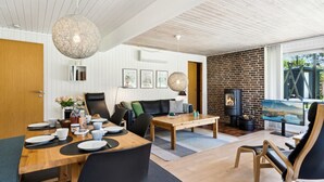 A modern living room with a wooden dining table, black chairs, a fireplace, and a large window with a view. - "Aleta" - 600m from the sea by Interhome (Grenaa)