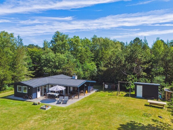 Una casa moderna con un patio amplio, un espacio de estar cubierto al aire libre y un cobertizo pequeño.