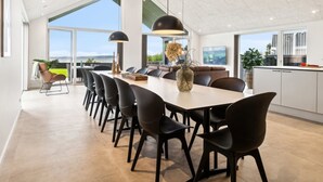 Un espace de salle à manger moderne avec une longue table, des chaises noires et des luminaires suspendus.