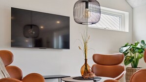 Un salon moderne doté d’un téléviseur à écran plat, de fauteuils en cuir, d’une table basse ronde et d’un luminaire suspendu.