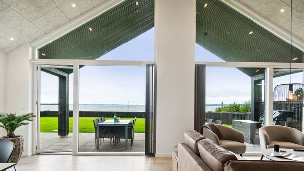 Un intérieur moderne doté d’une grande porte-fenêtre coulissante qui donne sur un patio extérieur offrant une vue sur la mer.
