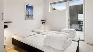 Une chambre moderne avec un grand lit, une fenêtre et un tableau représentant une scène de plage.