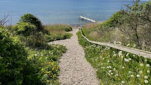 A gravel path leading to a wooden dock over water, surrounded by greenery and dandelions. - "Gedda" -  from the sea by Interhome (Vestervig)